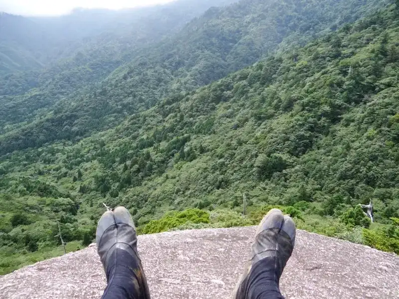 pes-de-caminhante-com-botas-de-trilha-sobre-penhasco-rochoso-com-vista-panoramica-da-floresta-verde-de-yakushima-no-japao