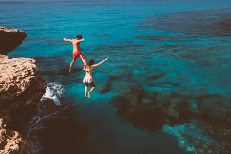 Junges mutiges Taucherpaar springt von einer Klippe ins Meer