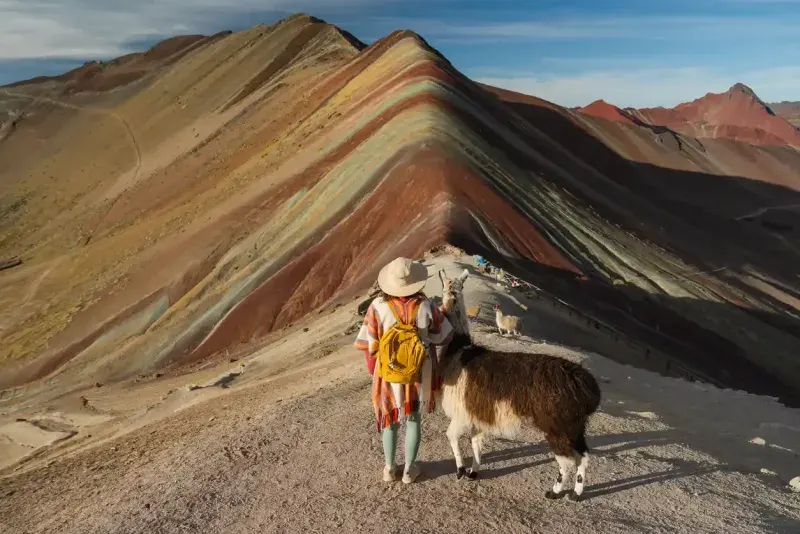 Woman with alpacas on the background of Rainbow mountain in Peru