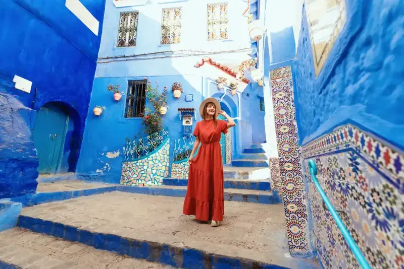 Young woman with red dress visiting the blue city Chefchaouen, Marocco