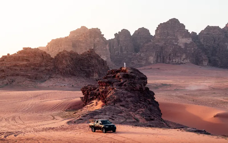 A black off-road pickup truck parked next to a massive rock formation in Wadi Rum