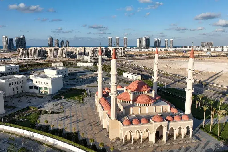 Weitwinkelaufnahme einer modernen islamisch geprägten Stadtarchitektur an der Küste mit urbaner Entwicklung am Meer.