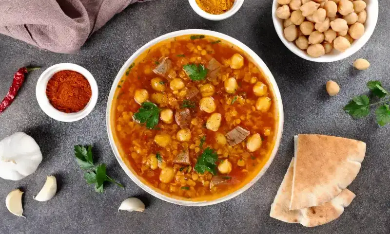 Moroccan harira soup with ingredients, spices and arabic bread on grey background. Ramadan iftar food.