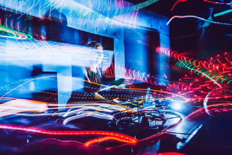 Junge Frau als DJ auf der Bühne, spielt Musik, bunte Lichter und Publikum im Hintergrund