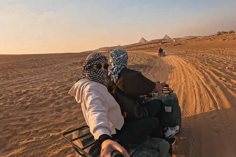 Due turisti si godono un giro in quad nel deserto, avvicinandosi alle maestose piramidi di Giza al tramonto.