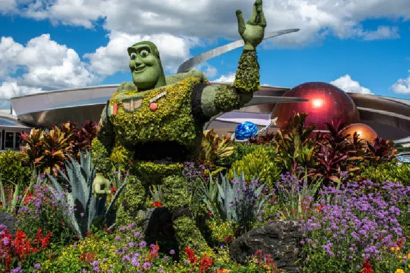 Bunte, kunstvoll gestaltete Pflanzenfiguren in Form von Disney-Charakteren beim EPCOT Flower & Garden Festival, umgeben von blühenden Blumen und grünem Gras.