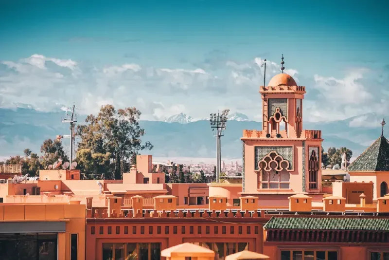Arquitectura tradicional marroquí con un minarete y las montañas del Atlas al fondo en Marrakech, Marruecos