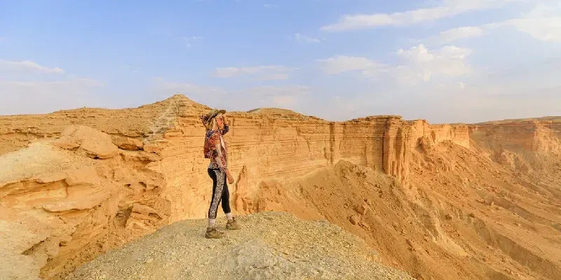La hora dorada ilumina a una turista en el borde del acantilado del mundo al atardecer, Arabia Saudita.