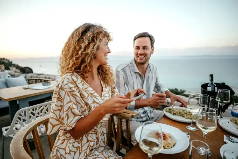Joven alegre tomando una foto de su plato mientras disfruta de una cena romántica con su esposo.