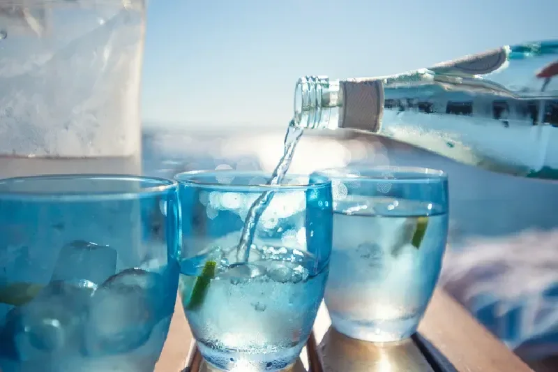 Wasser wird am Strand aus einer Flasche in ein Glas gegossen