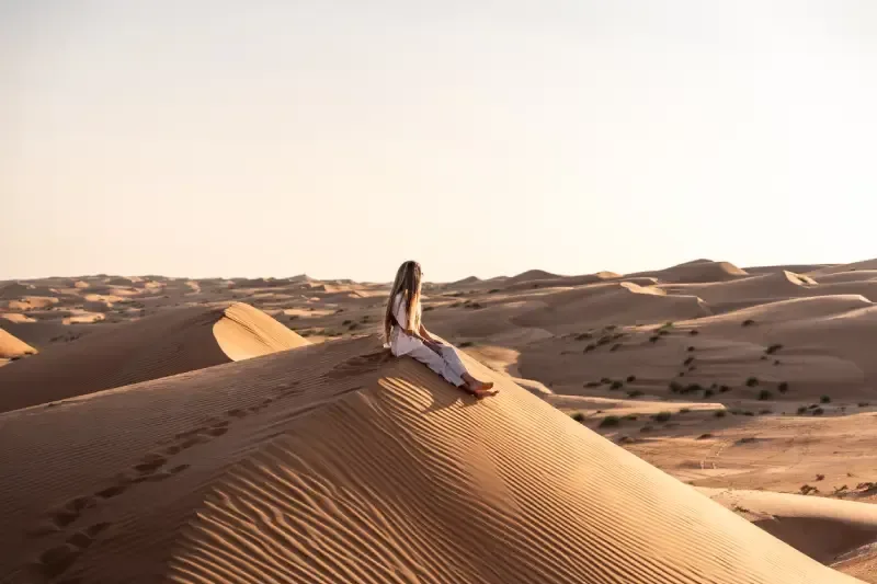 Giovane donna che si rilassa su una remota duna del deserto al tramonto, immersa nel vasto paesaggio dell’Oman.