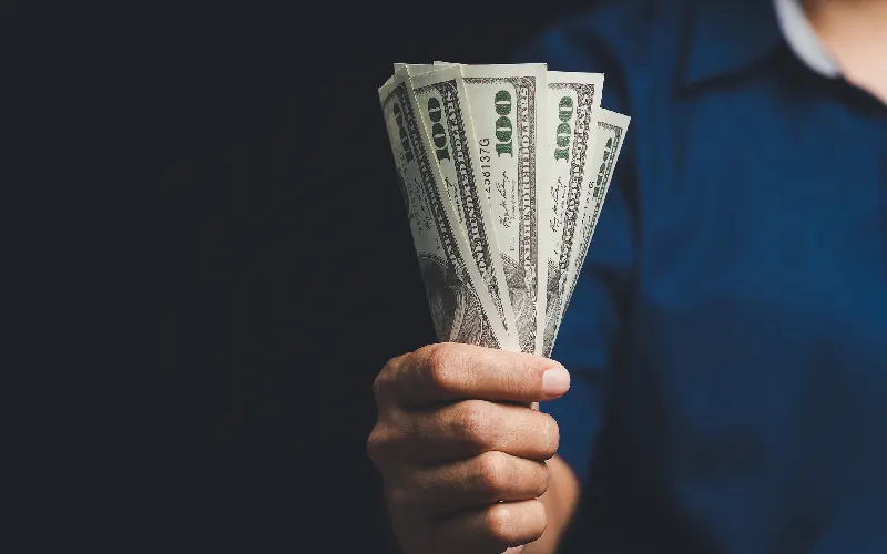 Close-up of a hand offering cash in a bundle of US dollars