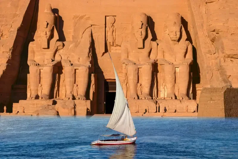 Una feluca tradizionale naviga sulle acque blu davanti al maestoso tempio di Abu Simbel in Egitto