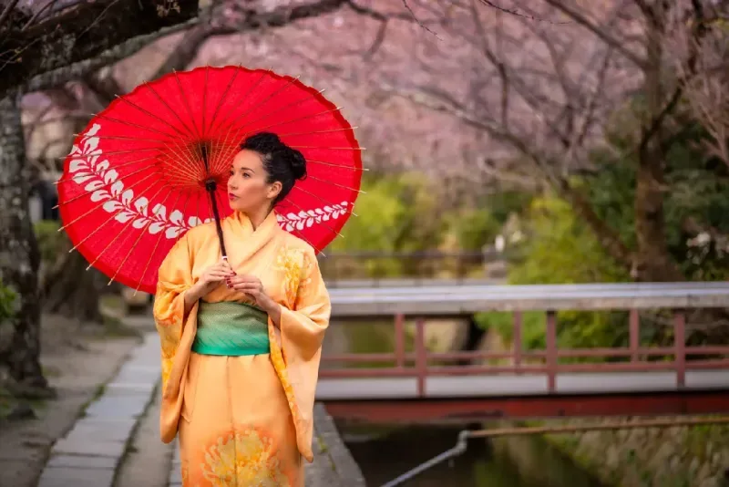 Mujer con kimono naranja y paraguas rojo en el Camino de la Filosofía en Kioto