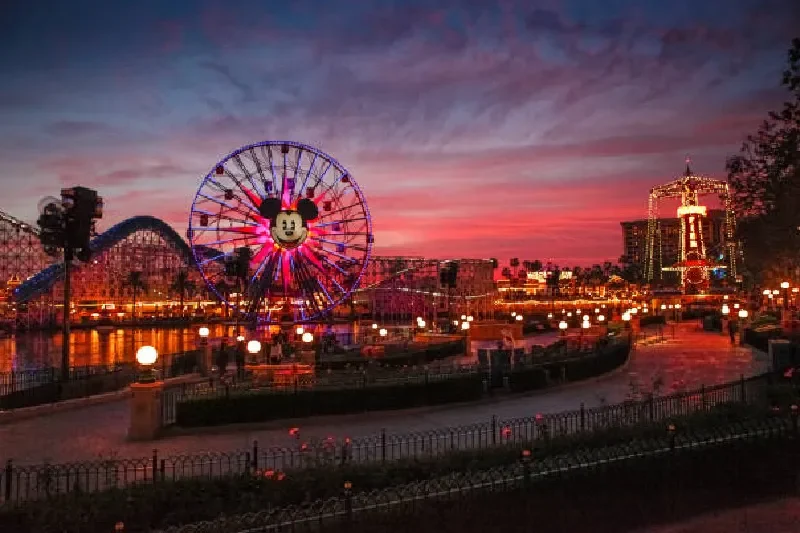 Blick auf den California Adventure Park während des Sonnenuntergangs, mit leuchtendem Himmel, Achterbahnen und Parkszenen.
