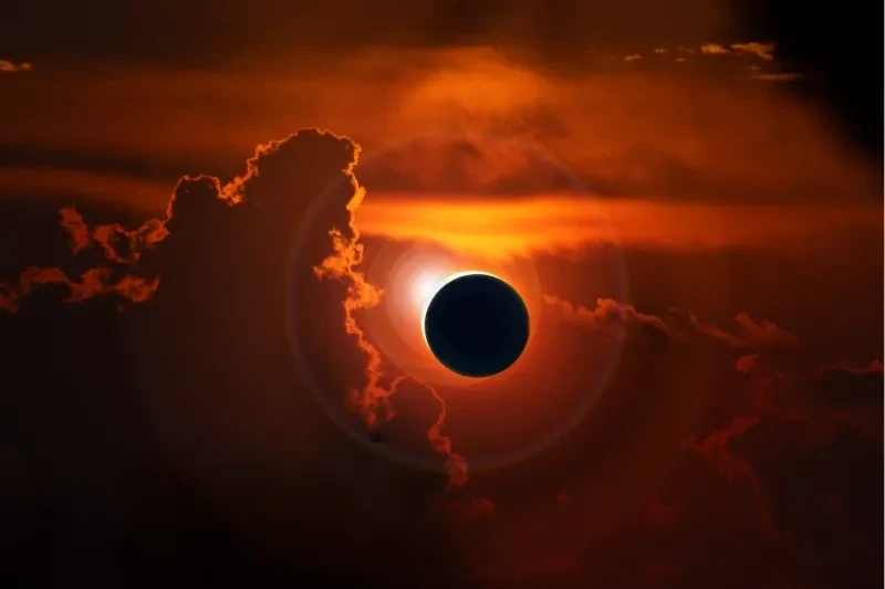 A total solar eclipse glowing through fiery orange clouds with a bright corona ring.