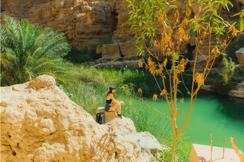 Viaggiatrice con zaino ammira il canyon di Wadi Ash Shab e il fiume verde smeraldo in Oman durante una giornata di sole.