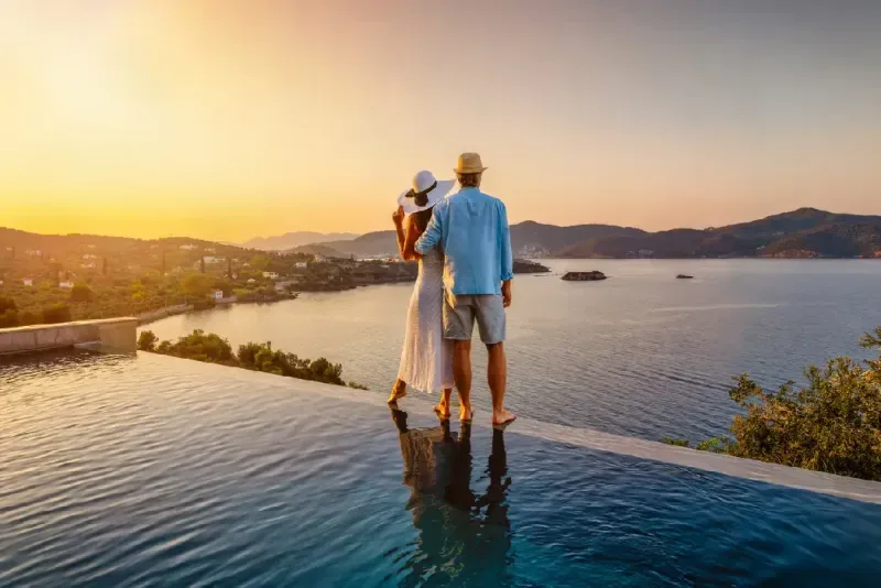 Una pareja romántica de vacaciones de verano junto a la piscina disfruta de una hermosa puesta de sol sobre el mar Mediterráneo.