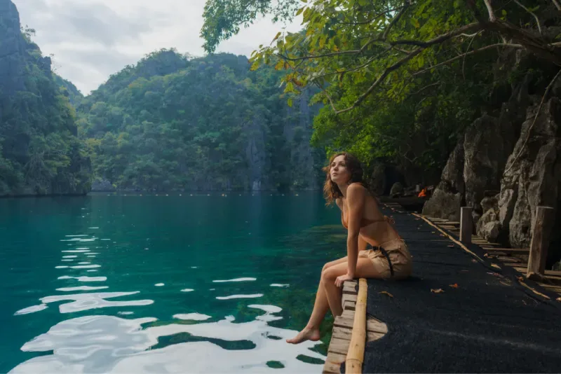 Woman enjoying the peaceful turquoise waters of Kayangan Lake in Coron with tropical forests and towering limestone cliffs.