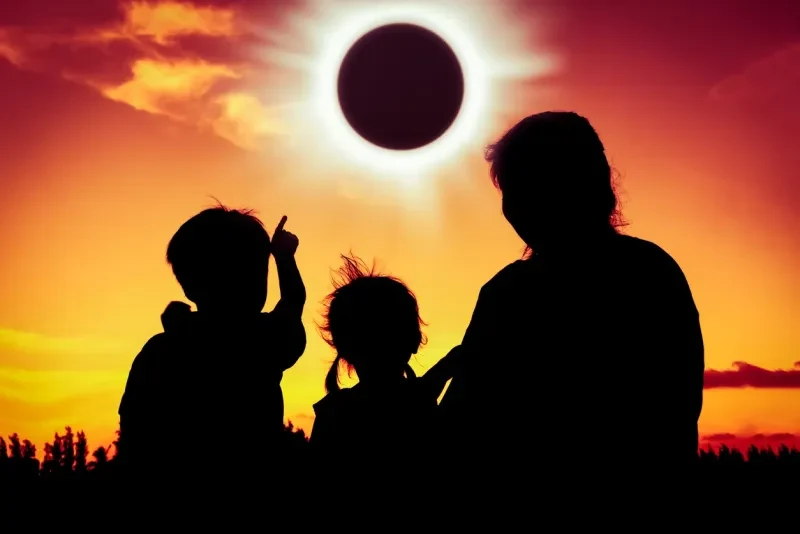 Family relaxing outdoors as a child points at the solar eclipse.