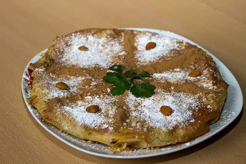 Chicken Bastilla, eine marokkanische Spezialität aus zartem Hähnchen, Blätterteig, Mandeln und Gewürzen, oft mit Puderzucker bestreut.