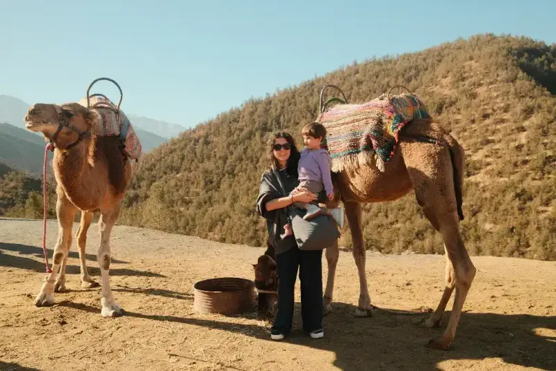 Madre sosteniendo a su hijo cerca de un camello en las montañas del Atlas.