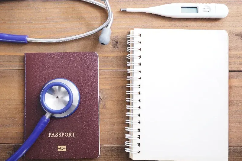 Nahaufnahme von Stethoskop, Reisepass, Thermometer und leerem Notizblock auf Holzuntergrund