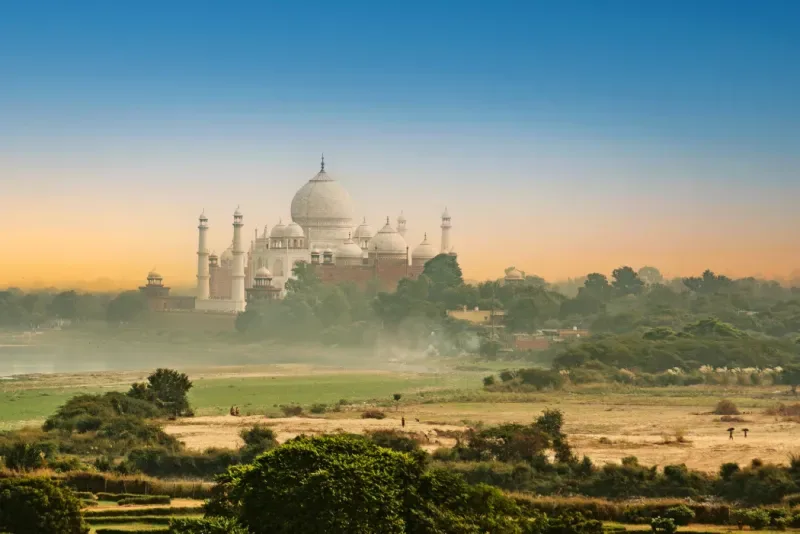 El Taj Mahal, con sus icónicas cúpulas, domina un paisaje exuberante bajo una vibrante puesta de sol.