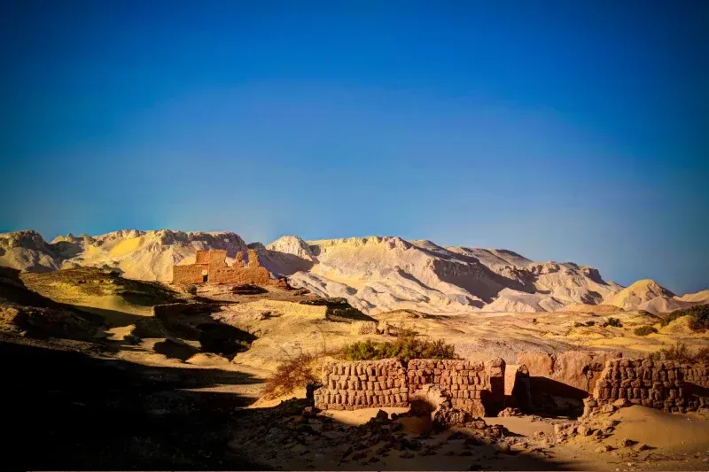Ruinen des römischen Tempels von Ain Lebekha in der Oase Kharga, Ägypten, mit Resten aus Stein inmitten der Wüstenlandschaft.