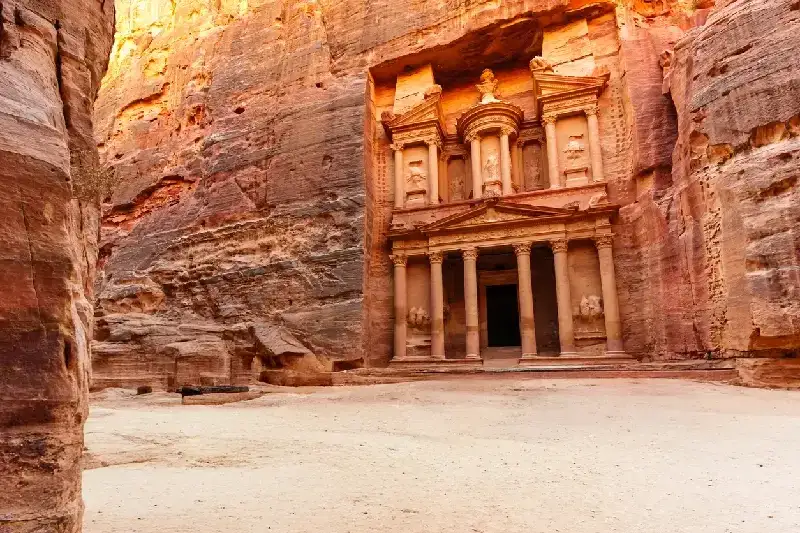 Die Ruinen des historischen Schatzhauses von Petra, in den Fels gehauen, in Jordaniens weiter Wüstenlandschaft im goldenen Licht des Sonnenuntergangs