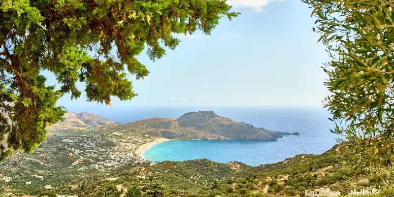 Un impresionante paisaje mediterráneo con una costa escarpada, un pueblo en la ladera y olivos.