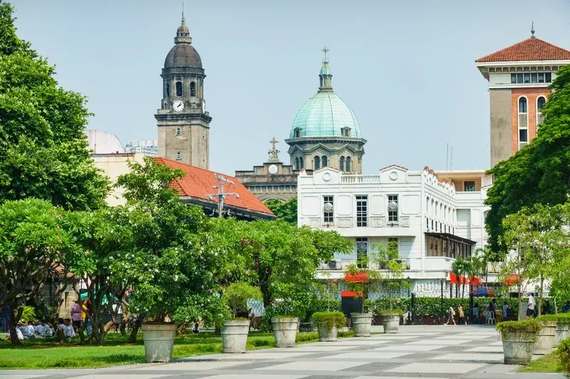 scenic-view-of-a-historic-intramuros-plaza-with-manila-cathedrals-green-dome-and-bell-tower-in-the-background-surrounded-by-white-colonial-era-buildings