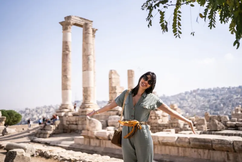 Visitor in light green jumpsuit standing before towering Roman columns at the Temple of Hercules in Amman with cityscape beyond.