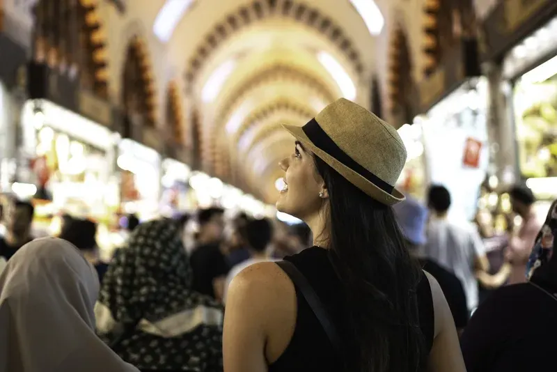 Smiling woman in a sun hat exploring the crowded, vaulted Spice Bazaar in Istanbul, Turkey