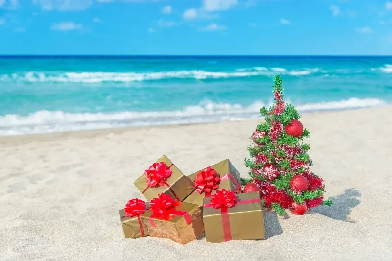 Weihnachtsbaum und viele Geschenkboxen an einem Sandstrand am Meer.