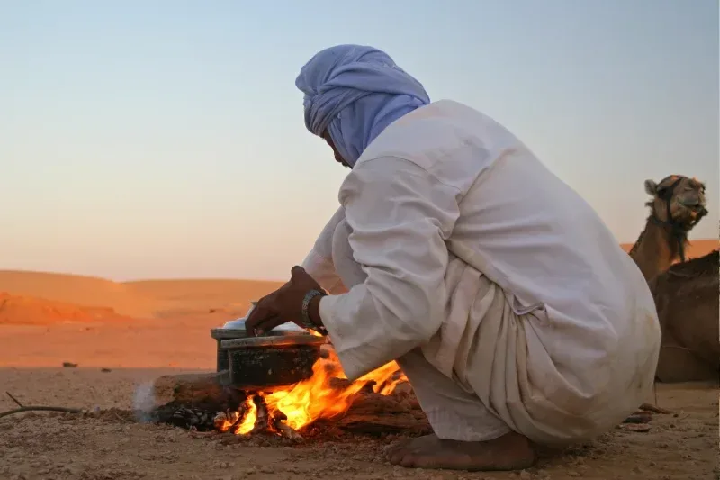 Beduine bereitet in der Wüste ein Abendessen über offenem Feuer zu.