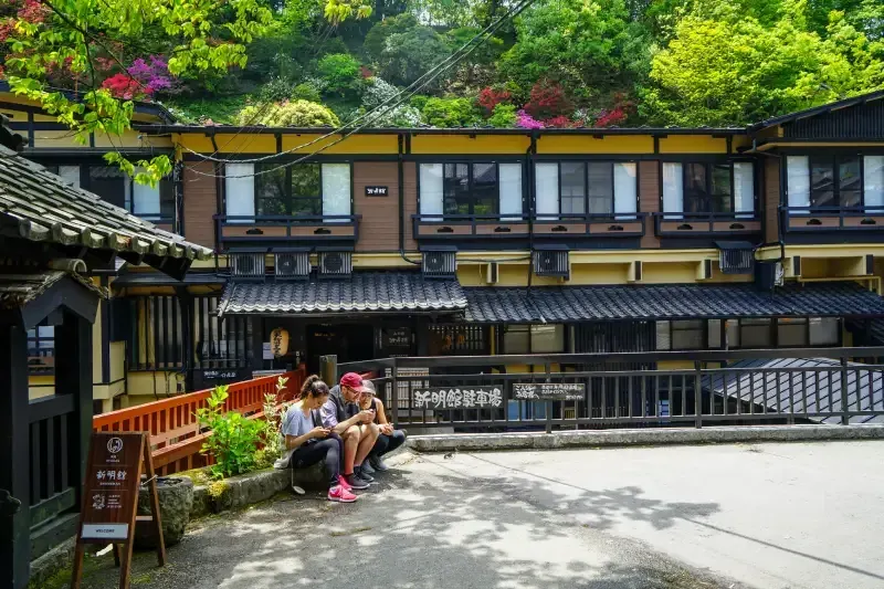 ryokan-tradicional-em-kurokawa-onsen-no-japao-com-pessoas-sentadas-em-frente-a-fachada-de-madeira-cercada-por-arvores-floridas