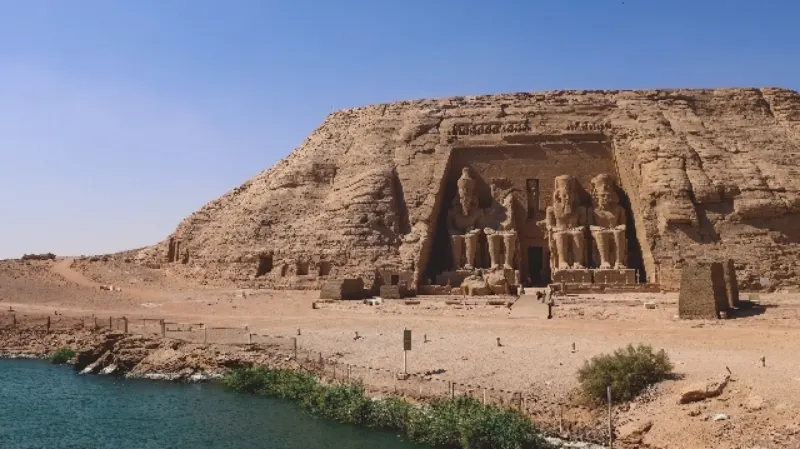The Great Temple of Abu Simbel overlooking Lake Nasser, featuring colossal statues of Ramses II carved into the rock façade under a bright blue sky.
