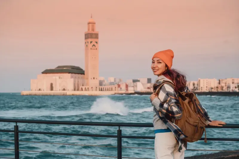 Young woman tourist with backpack enjoying the view of Hassan II Mosque in Casablanca, Morocco