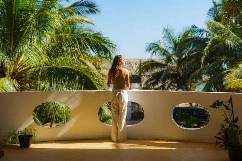 Una elegante mujer en el balcón al atardecer contempla las palmeras en un complejo turístico durante sus vacaciones tropicales.