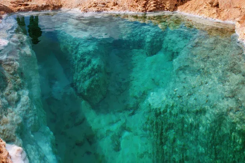 Salzpool in der Siwa-Oase, Ägypten, mit kristallklarem türkisfarbenem Wasser, das mineralische Formationen sichtbar macht