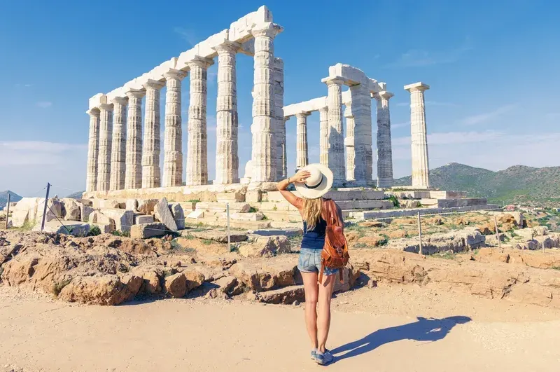 A female tourist is taking a photo in front of Temple of Poseidon at Cape Sounion at the edge of Attica