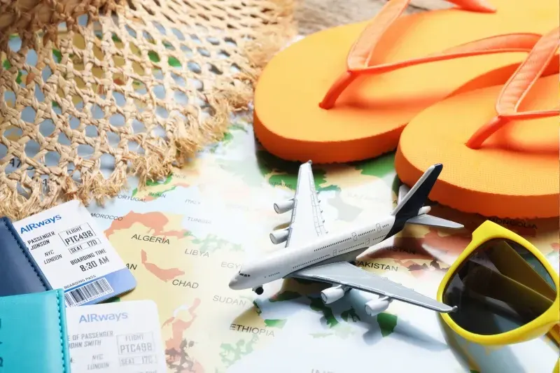Reisepässe, Flugtickets, Spielzeugflugzeug und Strandutensilien auf einer Weltkarte, Nahaufnahme