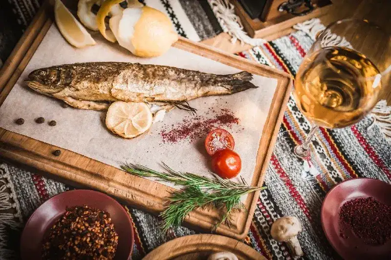Mediterrane Küche: Geräucherter Hering, serviert mit Frühlingszwiebeln, Zitrone, Kirschtomaten, Gewürzen, Brot und Tahini-Sauce auf dunklem Hintergrund. Draufsicht mit Nahaufnahme.