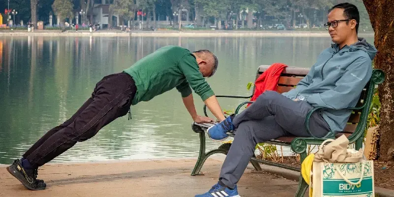  Un hombre vietnamita hace ejercicio mientras otro permanece sentado impasible junto al lago Hoan Kiem.