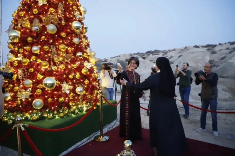Decorated Christmas tree with red and gold ornaments surrounded by visitors and photographers in desert setting.