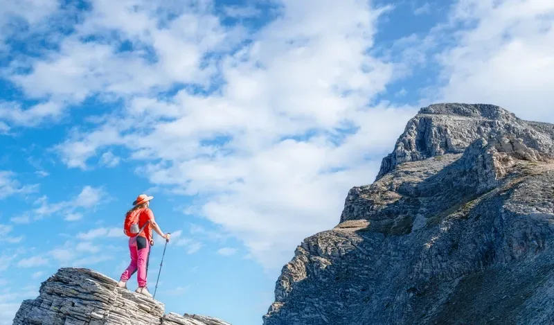 Female hiker with trekking poles standing on a rocky ridge looking toward a mountain summit in Turkey