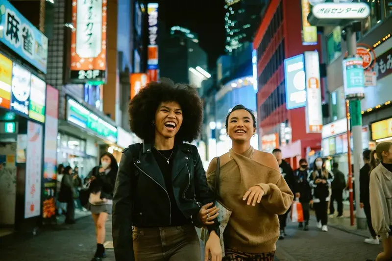 duas-mulheres-rindo-enquanto-caminham-por-uma-rua-iluminada-em-toquio