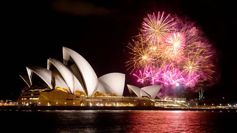 Buntes Feuerwerk über dem Sydney Opera House in Sydney bei Nacht, mit leuchtenden Farben, die den Himmel erhellen und sich im Wasser des Hafens spiegeln.