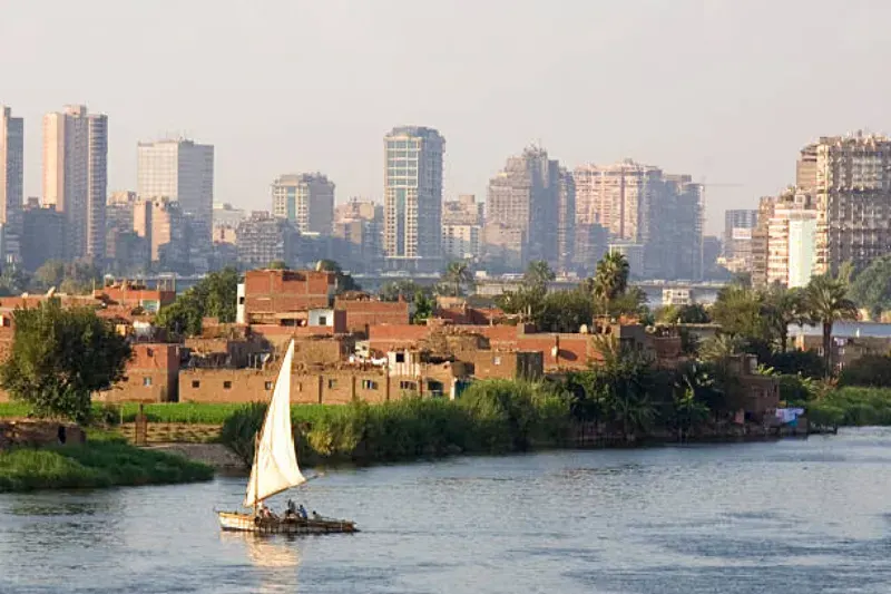 Traditionelle und moderne Boote fahren auf dem Nile River, mit spiegelndem Wasser, Uferlandschaften und dem goldenen Licht der Sonne, das die historische Atmosphäre des Flusses unterstreicht.